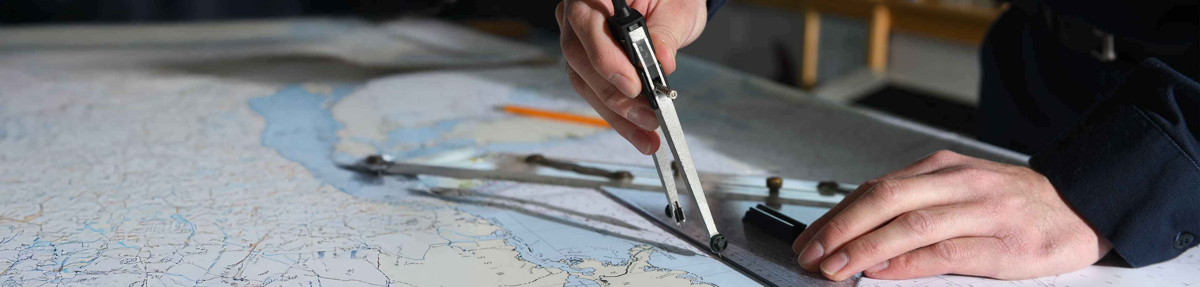 Close-up of a person's hands holding a compass and measuring on a nautical map